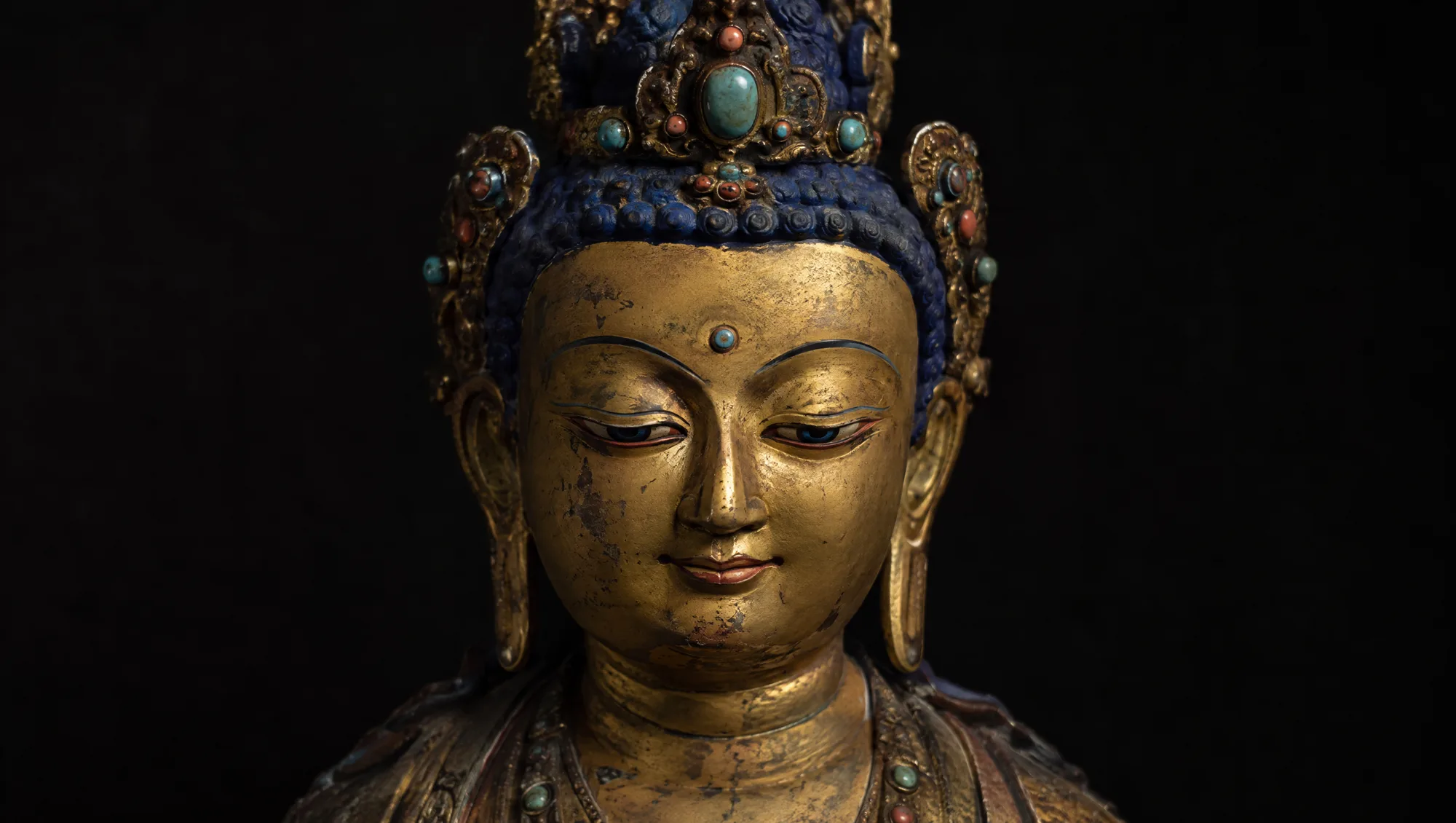 A Tibetan gilt-copper Buddha with a cold-gold face and turquoise in the crown