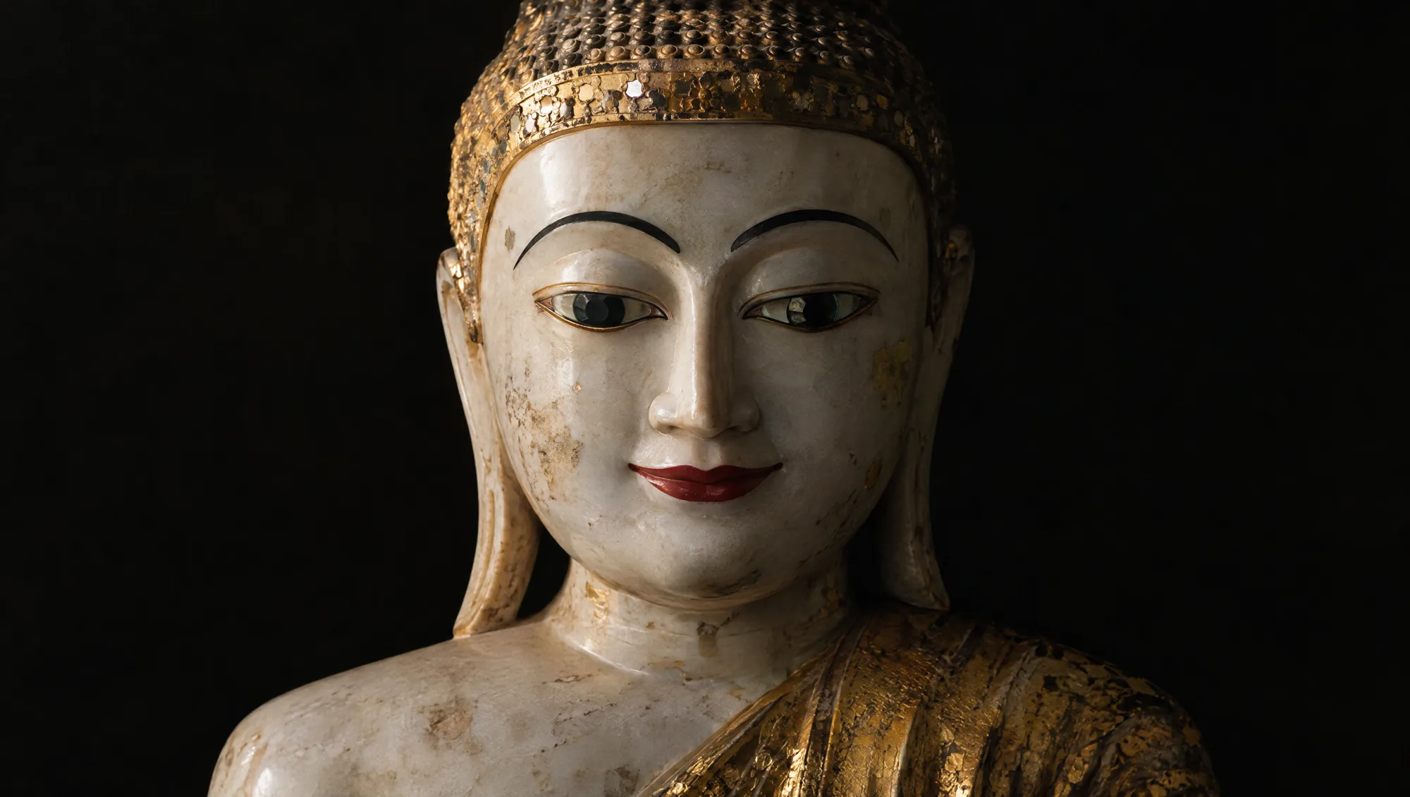 A Burmese marble Buddha with gold leaf on the robe and a red-painted mouth