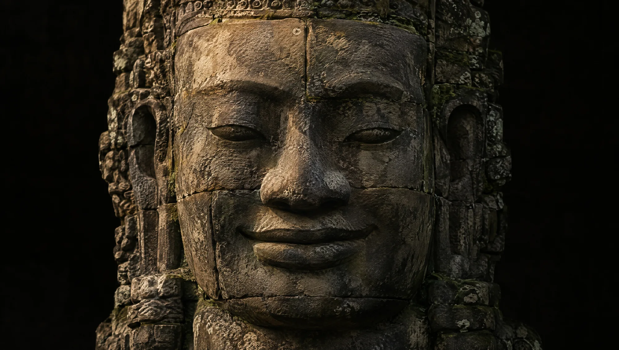 A giant Bayon stone face in weathered sandstone with moss in the joints